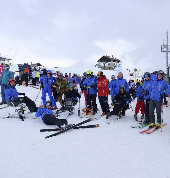 Group of people with ski and monoski equipment on the snow in the mountains with a cloudy sky.