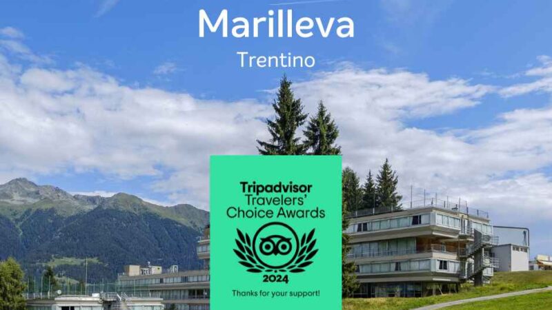 Obraz Marilleva, Trentino, z nagrodą Tripadvisor i górami w tle. Niebieskie niebo i zielona łąka na pierwszym planie.