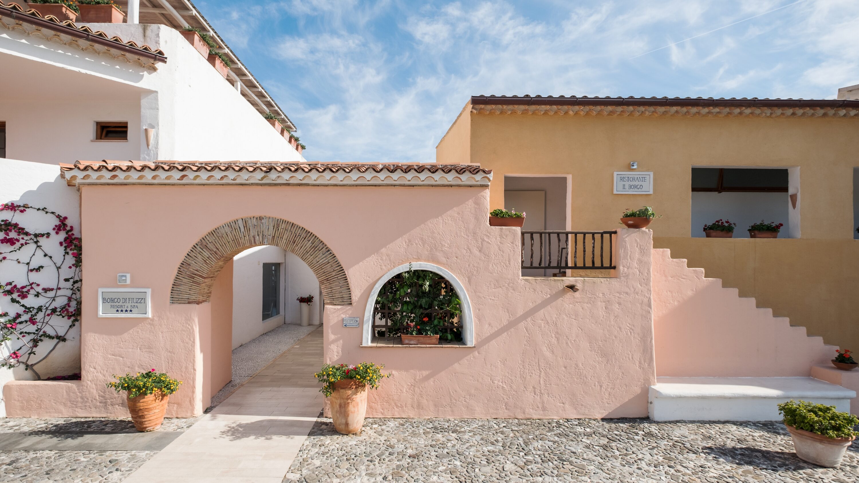 Edificio con facciate color pastello, piante e riccioli in pietra, sotto un cielo azzurro.