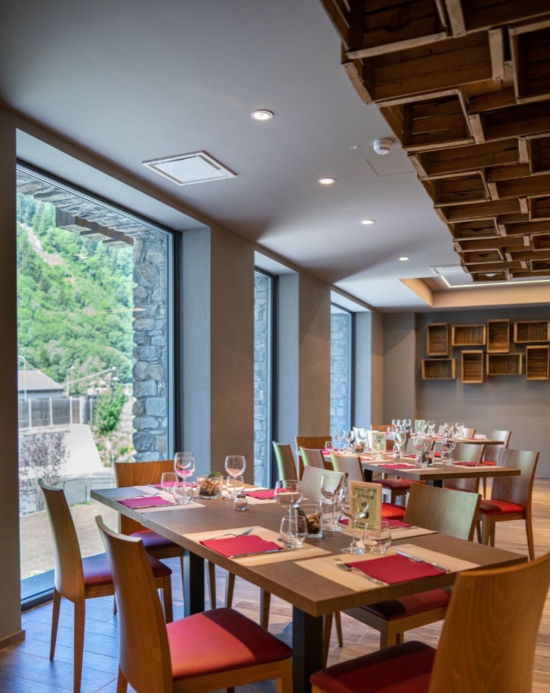 Sala da pranzo elegante con tavoli pronti, grandi finestre e vista sulla natura circostante.
