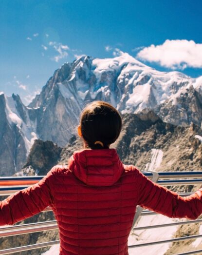 Person in a red jacket admiring the snow-covered mountains and the blue sky from the observatory.