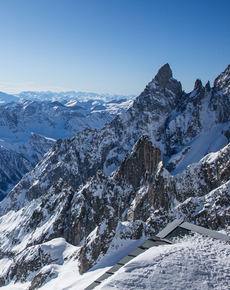 Panorama montano innevato con picchi aguzzi sotto un cielo sereno e azzurro. Neve fresca ricopre il paesaggio.