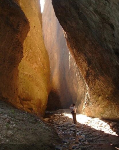 Osoba obserwująca oświetlone ściany skalne wewnątrz wąskiej naturalnej wąwozu.