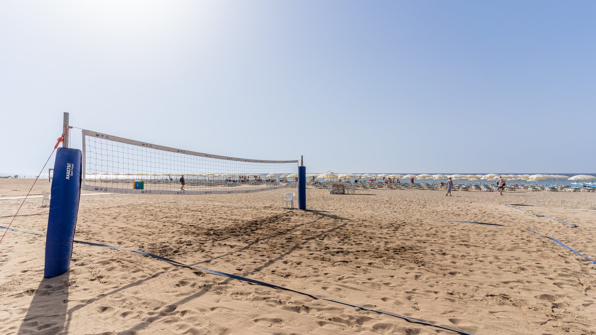 Pusty plac do siatkówki plażowej na piaszczystej plaży z białymi parasolami i bezchmurnym niebem.