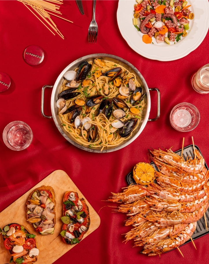 Piatto di spaghetti con frutti di mare, gamberi grigliati e antipasti di pesce su un tavolo rosso.