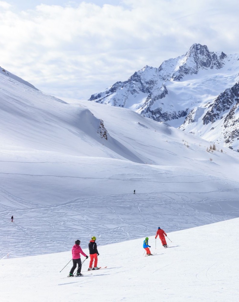 Sciare in una valle innevata con montagne e cielo nuvoloso sullo sfondo.