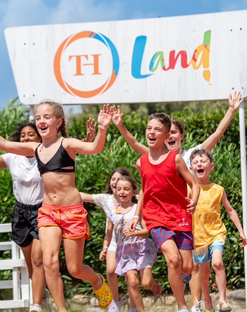 Bambini felici che corrono all’aperto con un cartello colorato di "TH Land!" sullo sfondo.