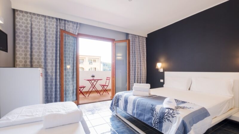 Vista di una camera da letto con letto matrimoniale, asciugamani e accessori, e balcone con sedie e tavolino.