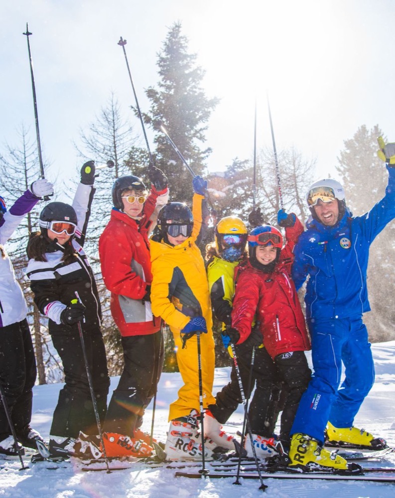Gruppo di sciatori sorridenti in abbigliamento colorato, accanto a alberi innevati, mentre festeggiano al sole.