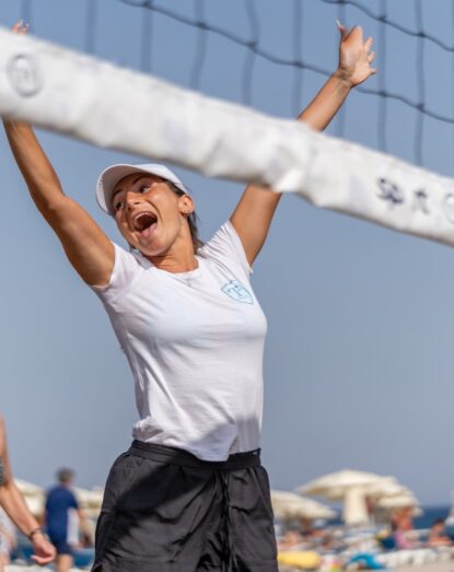 Szczęśliwa Donna grająca w siatkówkę plażową na plaży z siatką i parasolami w tle.