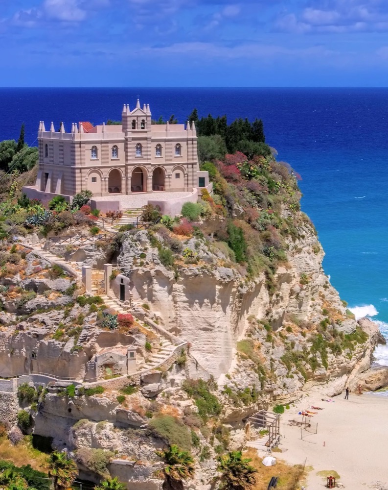 Santuario sulla scogliera vista mare a Tropea, con spiaggia sottostante e vegetazione mediterranea.