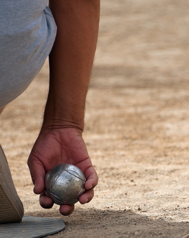 Persona che tiene una palla d'acciaio caduta a terra su terreno sabbioso.