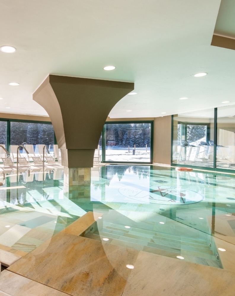 Interno di una piscina naturale con illuminazione soffusa e grandi finestre che lasciano entrare la luce naturale.