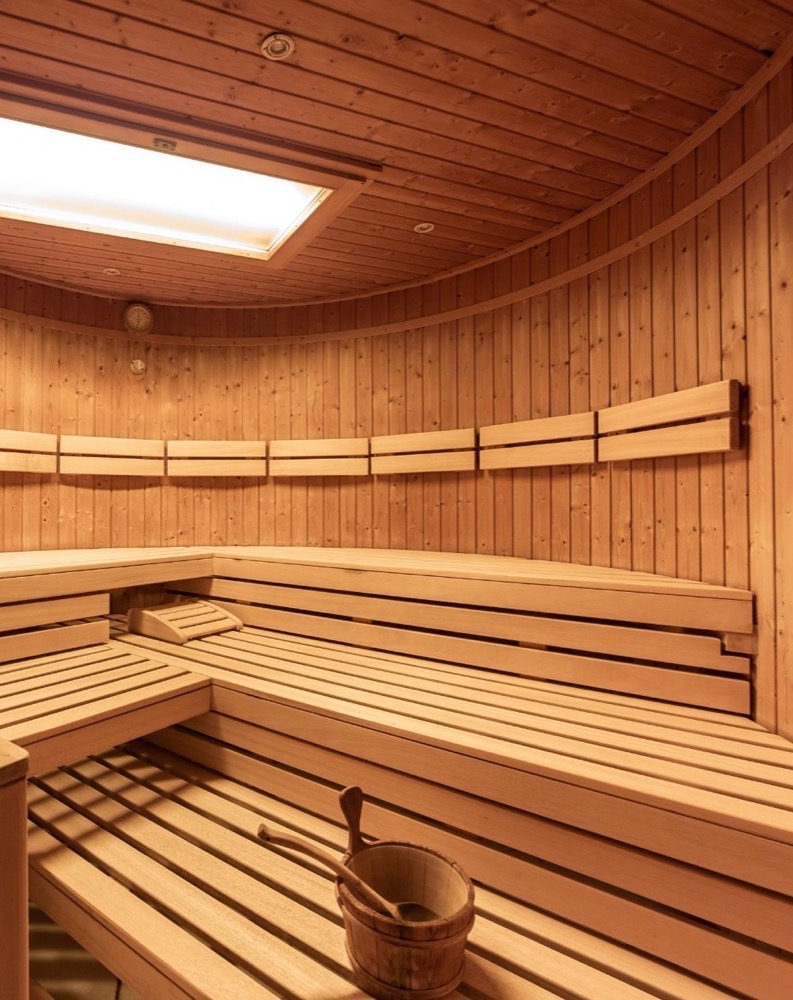 Interno di una sauna in legno con panche e bacinella per il vapore sotto un grande lucernario.