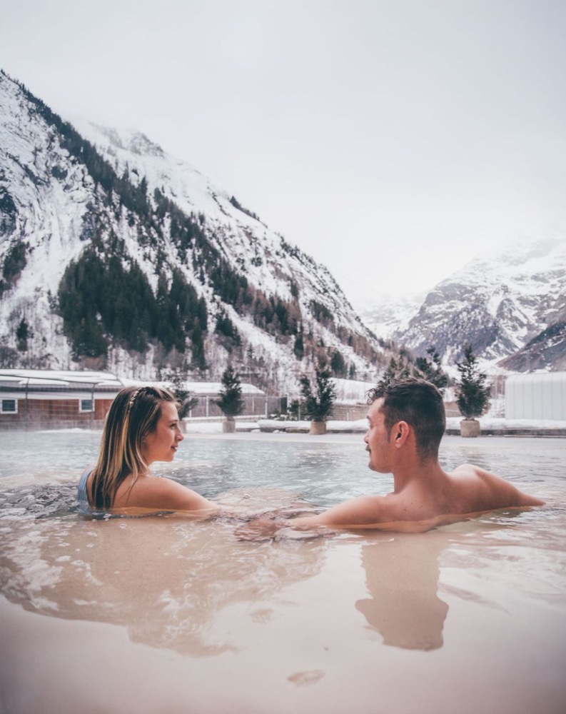Coppia che si rilassa in una piscina termale con montagne innevate sullo sfondo.