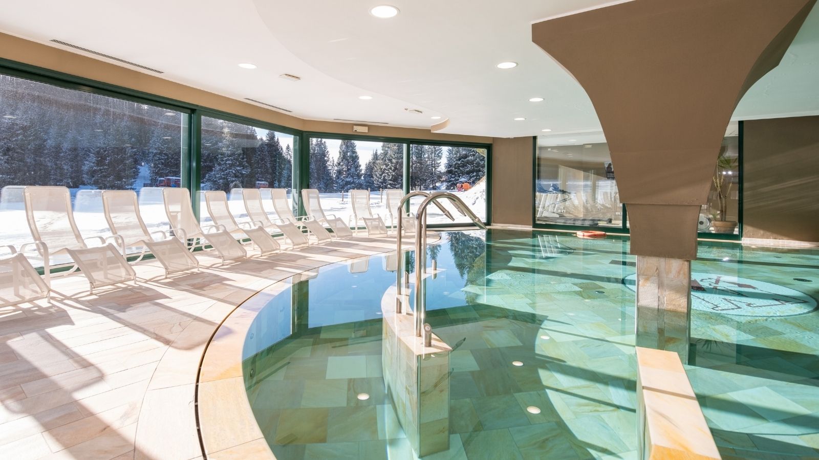 Indoor pool with chairs at the edge, large windows with views of the snow and snowy landscapes.