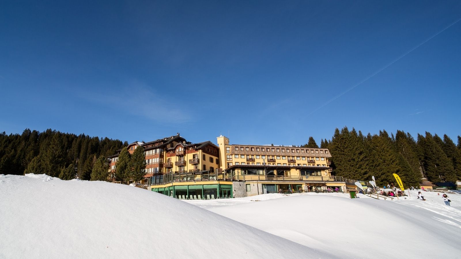 Colorful hotel among the trees with snow and bright blue sky above.