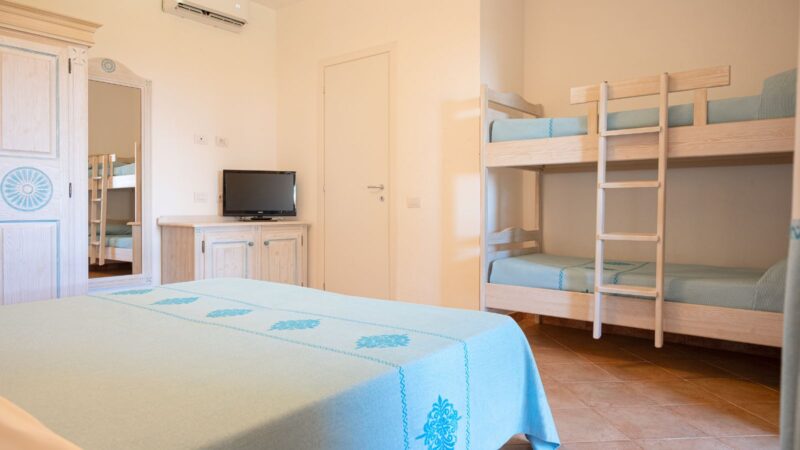 Camera con letto matrimoniale, letto a castello in legno chiaro, armadio, TV e aria condizionata, con biancheria azzurra.