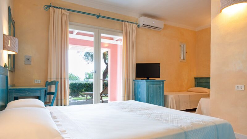 Camera da letto con letto matrimoniale e singolo, mobili azzurri, aria condizionata e porta finestra con vista giardino.