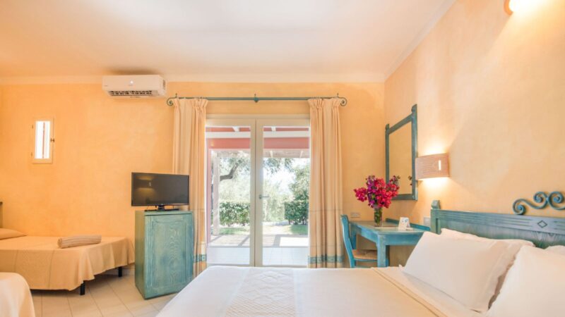 Camera doppia con letto matrimoniale e singolo, mobili turchesi, fiori rosa e porta finestra con vista giardino.