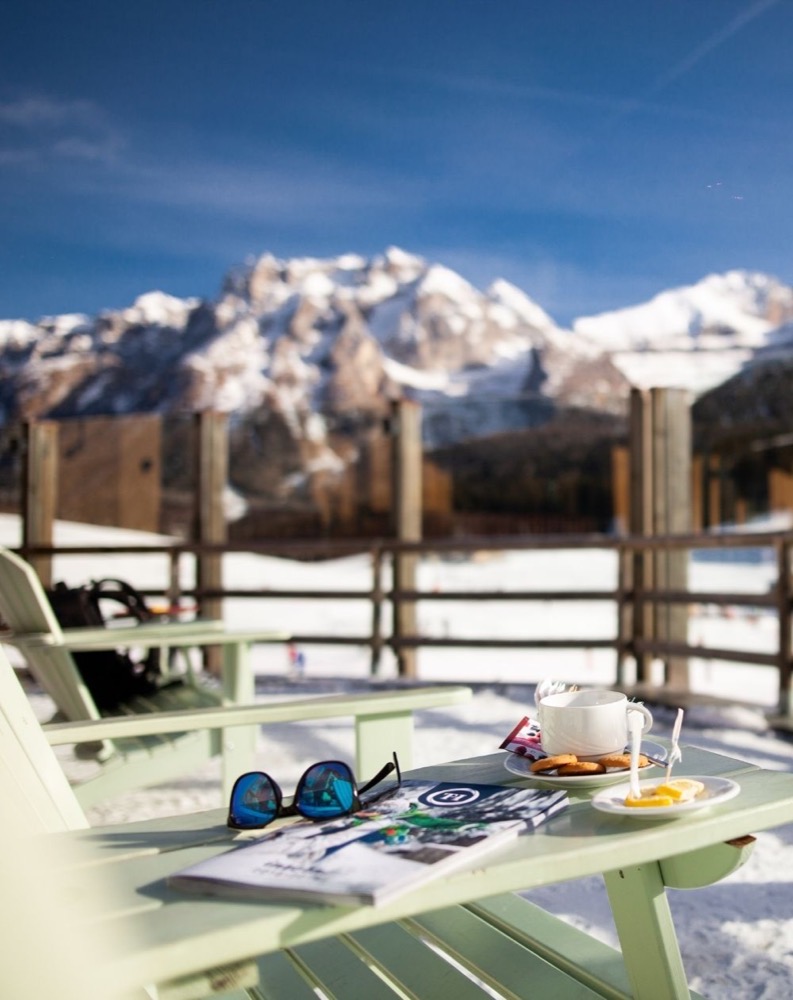 Coppia di occhiali da sole e colazione con vista sulle montagne innevate e cielo brumoso.