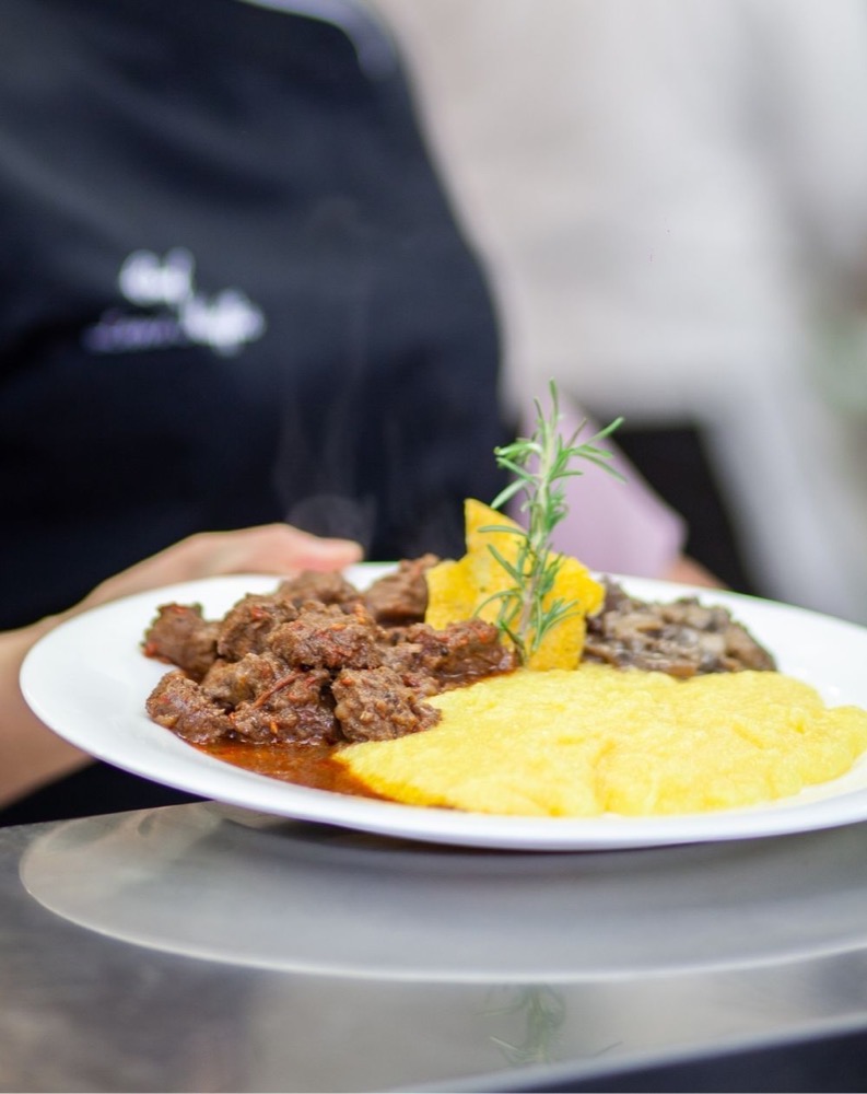 Piatto di carne in umido con polenta e guarnito con rametto di erbe aromatiche.
