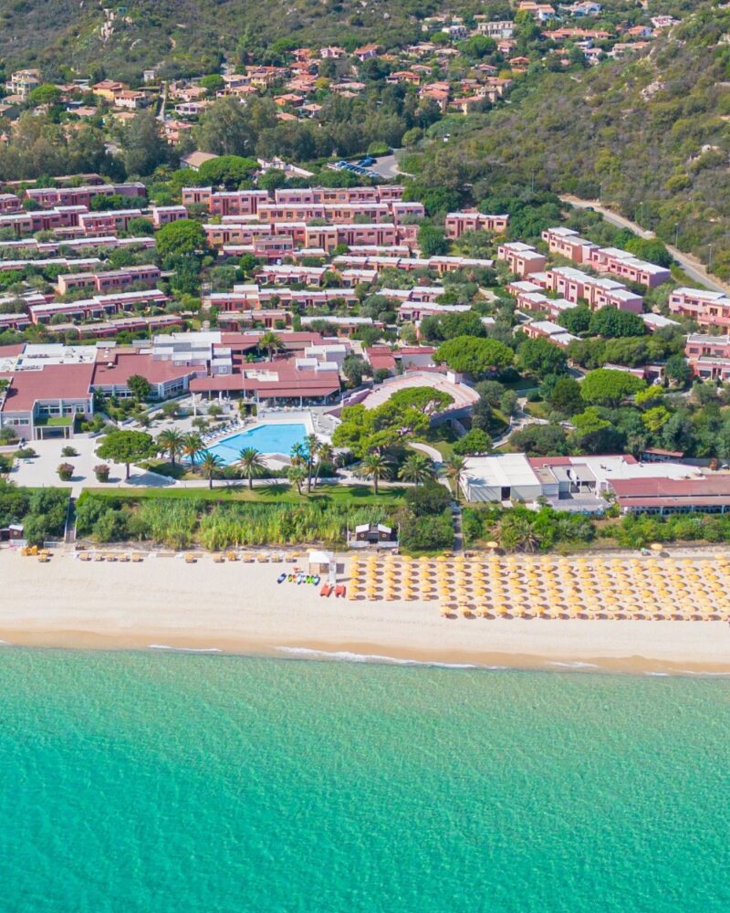 Vasta vista aerea di un resort sul mare, con una piscina e una spiaggia attrezzata di lettini e ombrelloni gialli.