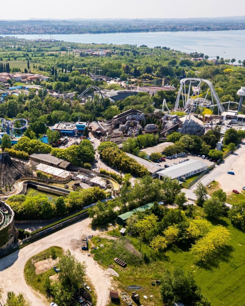 Parco divertimenti con montagne russe e attrazioni immerse nel verde vicino a un grande lago.