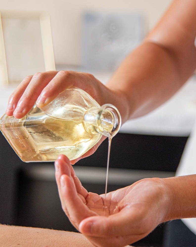 Mani che versano olio trasparente da una bottiglia di vetro.