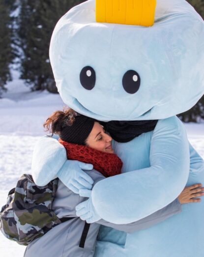 A woman embraces a masked character with a cloud head and yellow horn in a snowy environment.