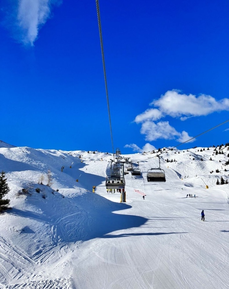 Sci alpino con seggiovia tra le piste innevate e cielo azzurro.