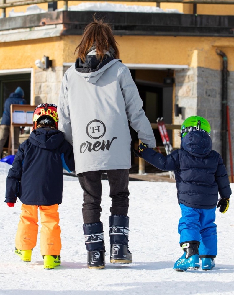 Animatori con bambini sugli sci in stazione sciistica, vista da dietro.