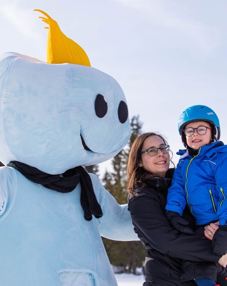 Persona in costume di una nuvola sorridente con una fetta di limone sulla testa, con donna e bambino in abbigliamento invernale.