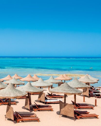 Spiaggia con lettini e ombrelloni di paglia, mare turchese e cielo sereno. Atmosfera rilassante e tropicale.