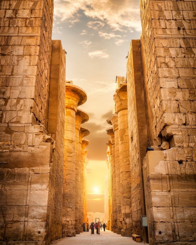 Vicolo tra grandi colonne di pietra, al tramonto, con visitatori che ammirano il sito storico.