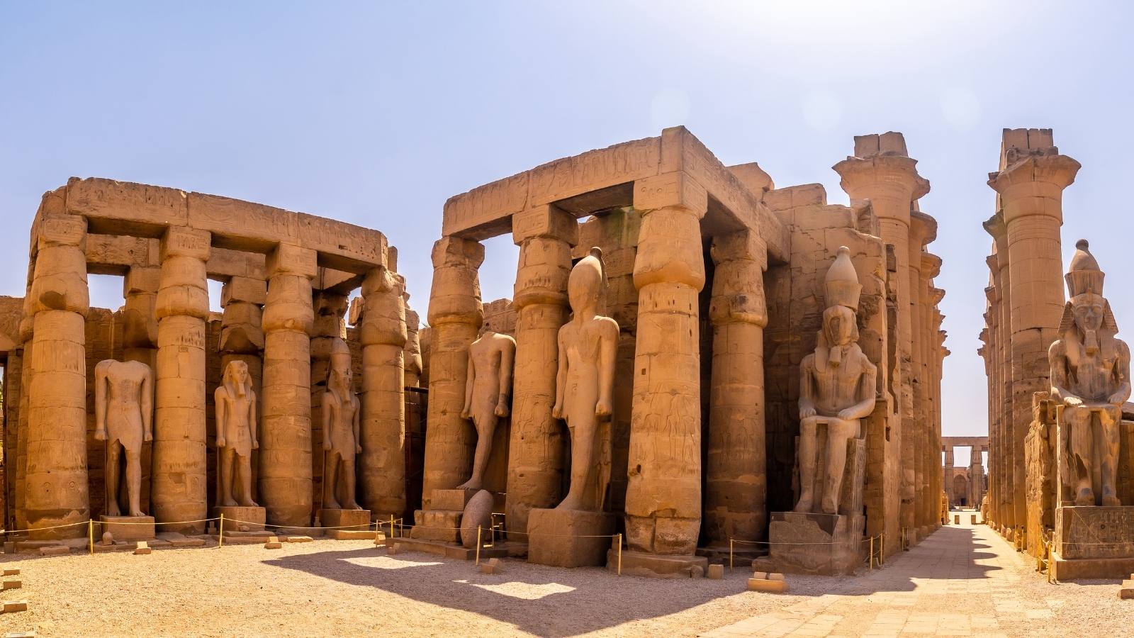 Tempio di Luxor, con colonne imponenti e statue di divinità egiziane, illuminate dalla luce solare.