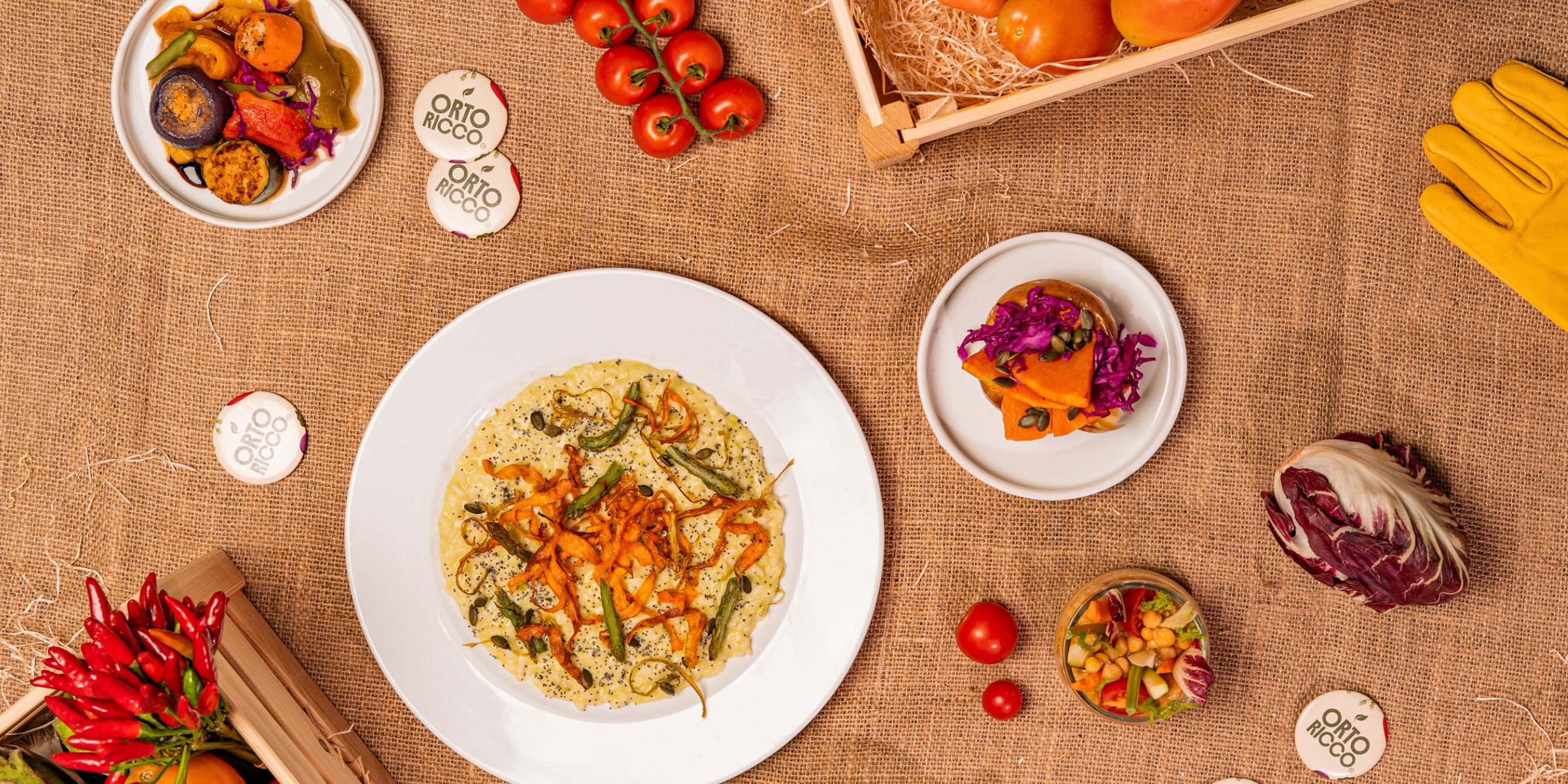 Piatti di cucina vegetariana con verdure fresche e cotte, pomodori, radicchio e peperoncini su tavolo rustico in juta.
